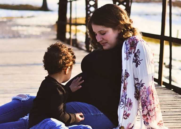 iowa surrogate mother with bipoc toddler holding surrogacy pregnant belly. Picture from surrogacy maternity shoot.